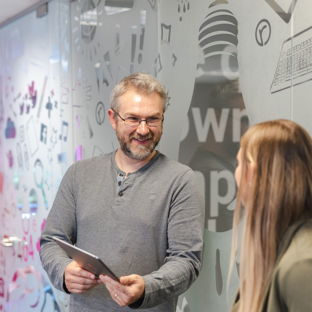 A marketer showing agency work on an iPad to another employee in the office | Reech