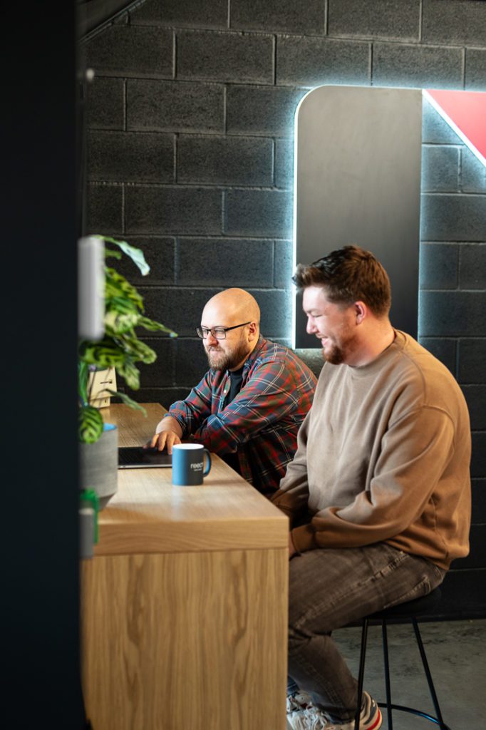 Pair of the development team collaborating by high desk near Reech sign – Reech Agency