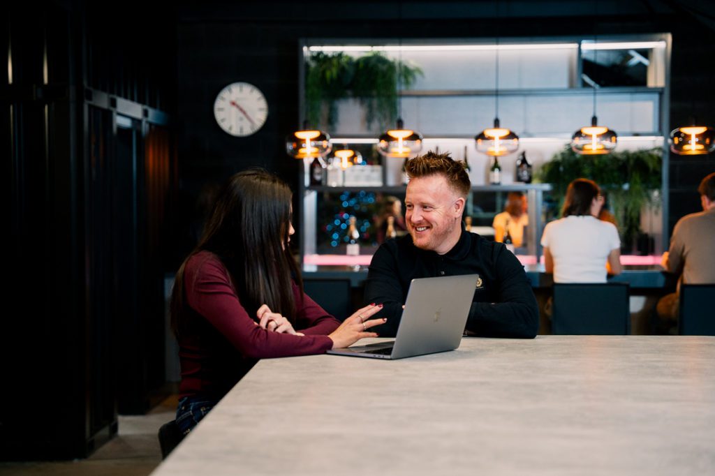 Two marketing team members discussing project details on laptop - Reech Agency