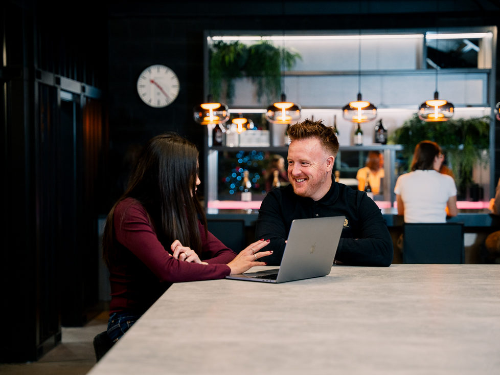 Two marketing team members discussing project details on laptop - Reech Agency