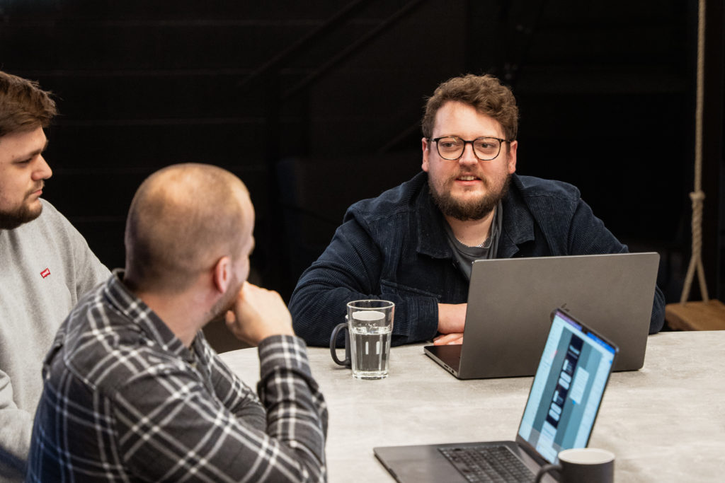 A team of web developers collaborating around a table with laptops during a meeting about custom integrations.