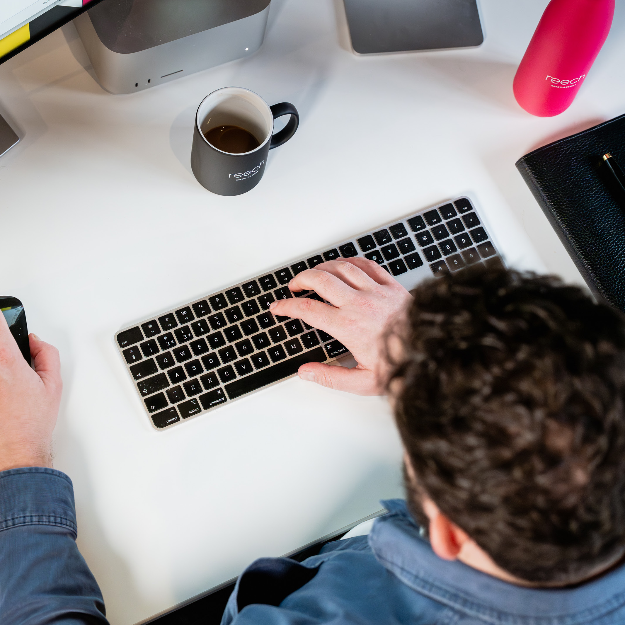 top-down shot of a marketing agency team member working at a clear white desk with a coffee mug, notebook, and smartphone